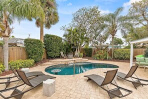 A backyard with a swimming pool, lounge chairs, and a wooden deck. - Evergreen (New Smyrna Beach)