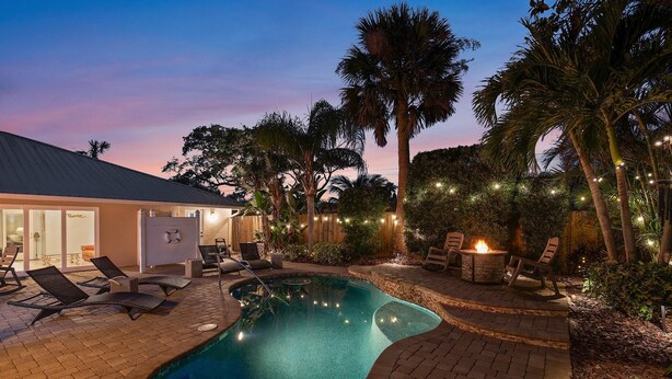 A swimming pool with lounge chairs and a fire pit area, surrounded by palm trees and a house. - Evergreen (New Smyrna Beach)