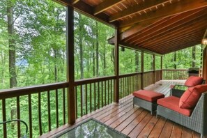 A covered outdoor deck with wooden railings, wicker furniture, and a glass table. - Breezy Bear, Ellijay, Ga (Ellijay)