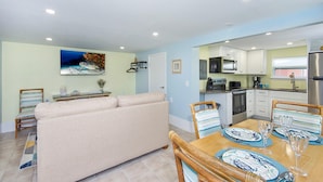 A modern kitchen with white cabinets, a stainless steel refrigerator, and a dining area with striped chairs and blue and white plates. - Island Paradise 6 (Fort Myers Beach)