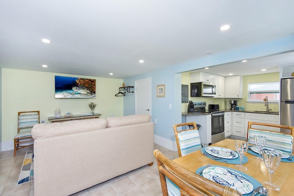 A modern kitchen with white cabinets, a stainless steel refrigerator, and a dining area with striped chairs and blue and white plates.