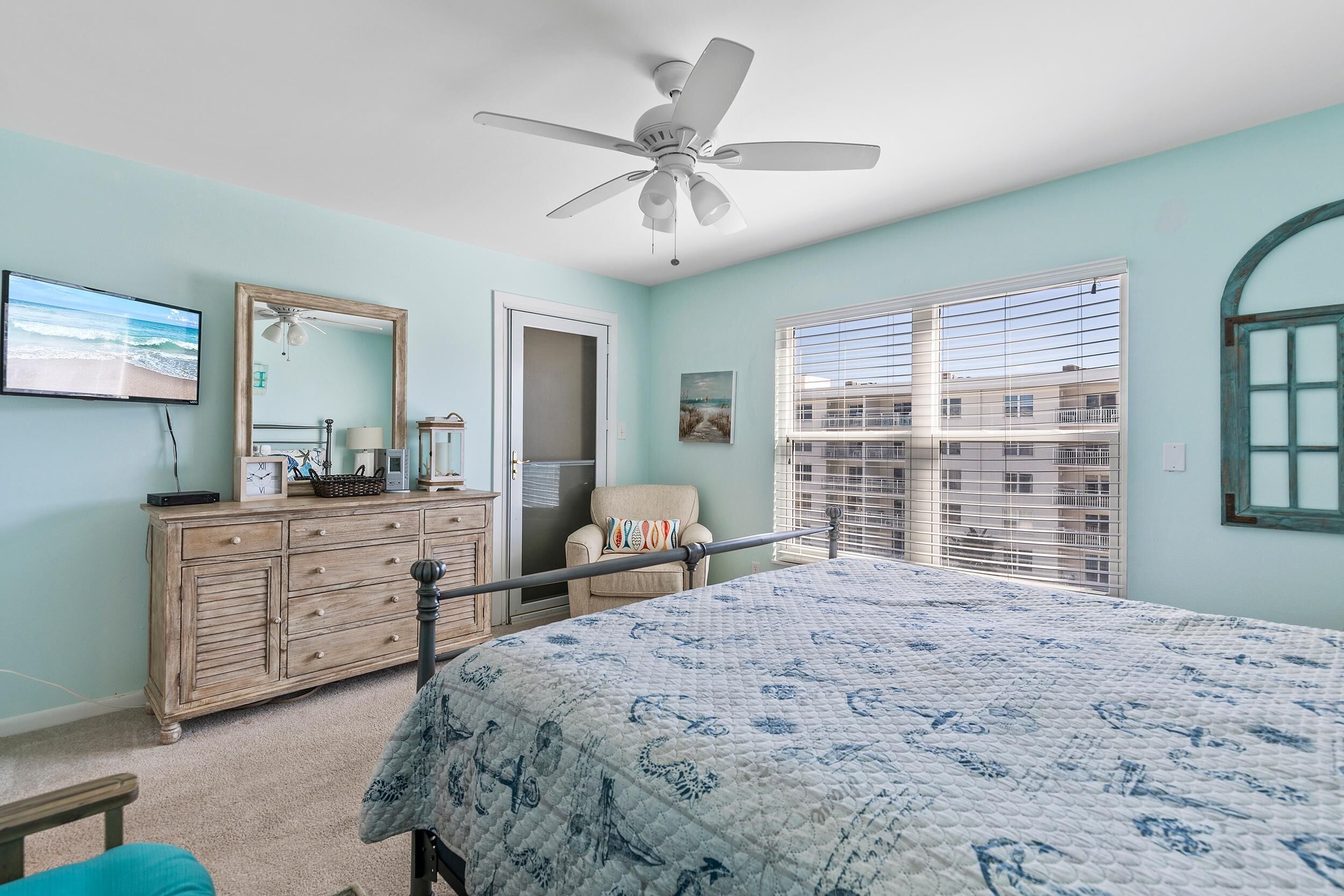 Un dormitorio con cama, cómoda, ventilador de techo, ventana grande y puerta.