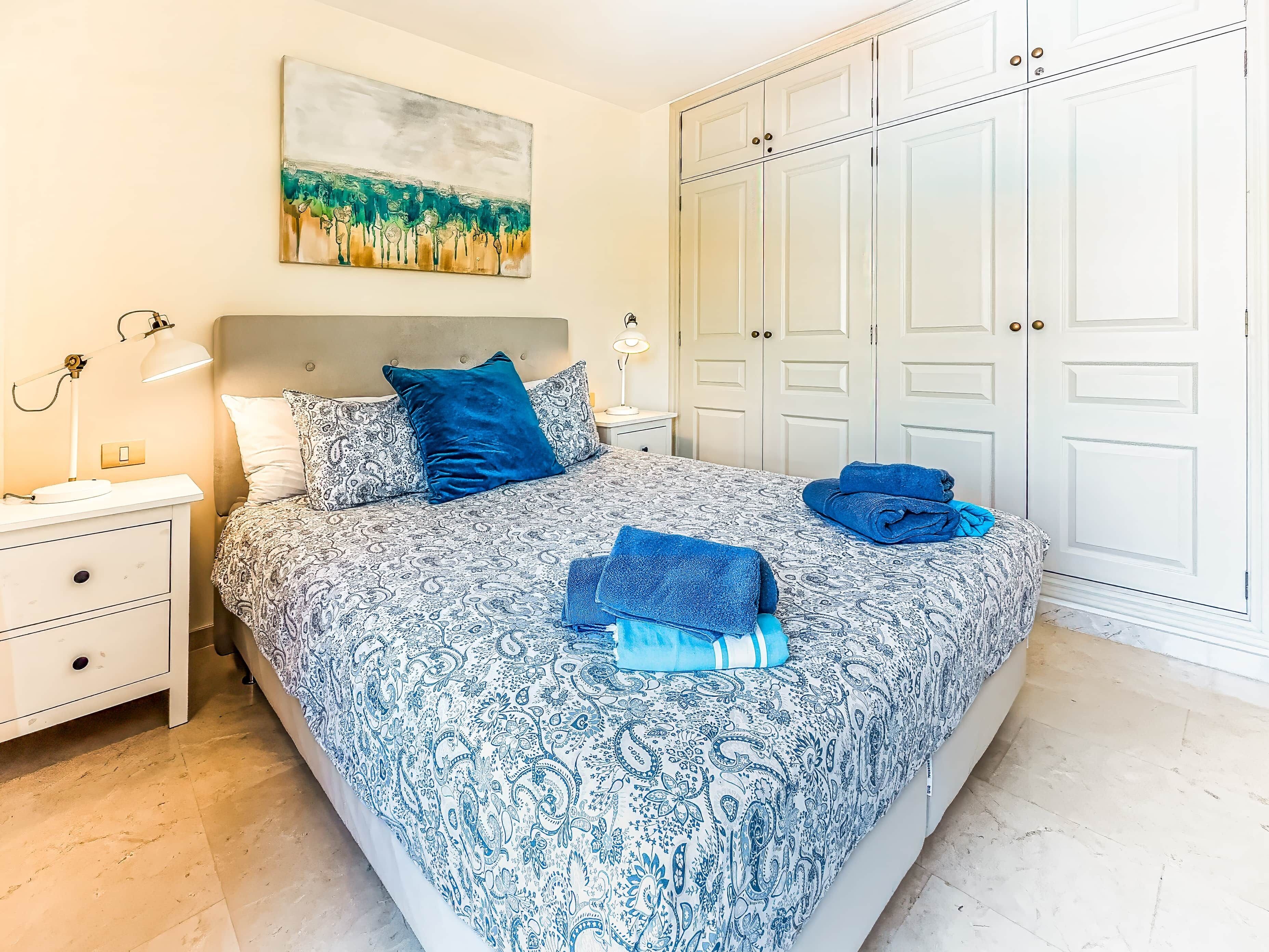 A bedroom with a bed, nightstands, a painting, and a wardrobe.
