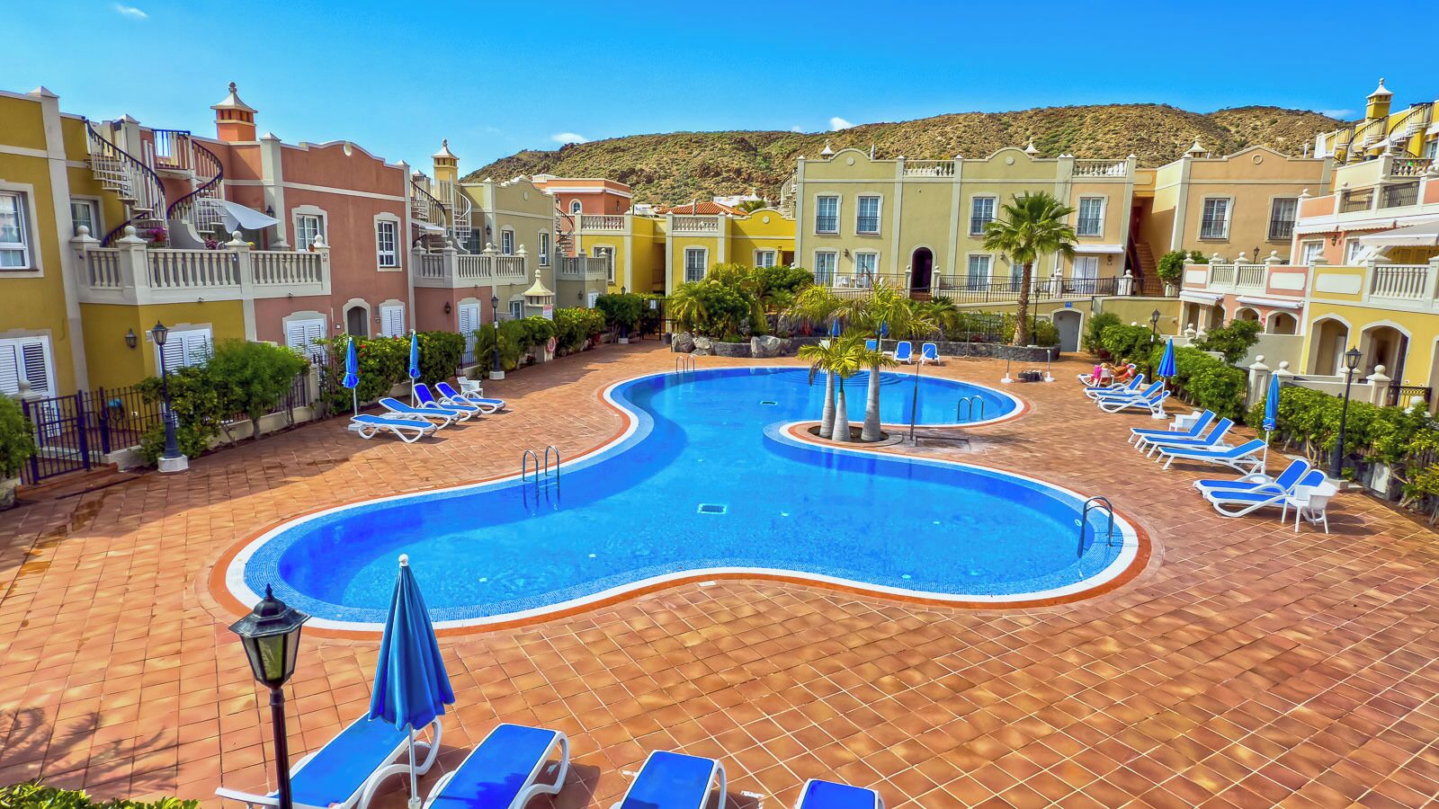 A swimming pool with sun loungers and a tiled deck.