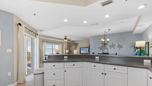 A modern kitchen with white cabinets, granite countertops, and a ceiling fan. - Oceanwalk 8-507 (New Smyrna Beach)
