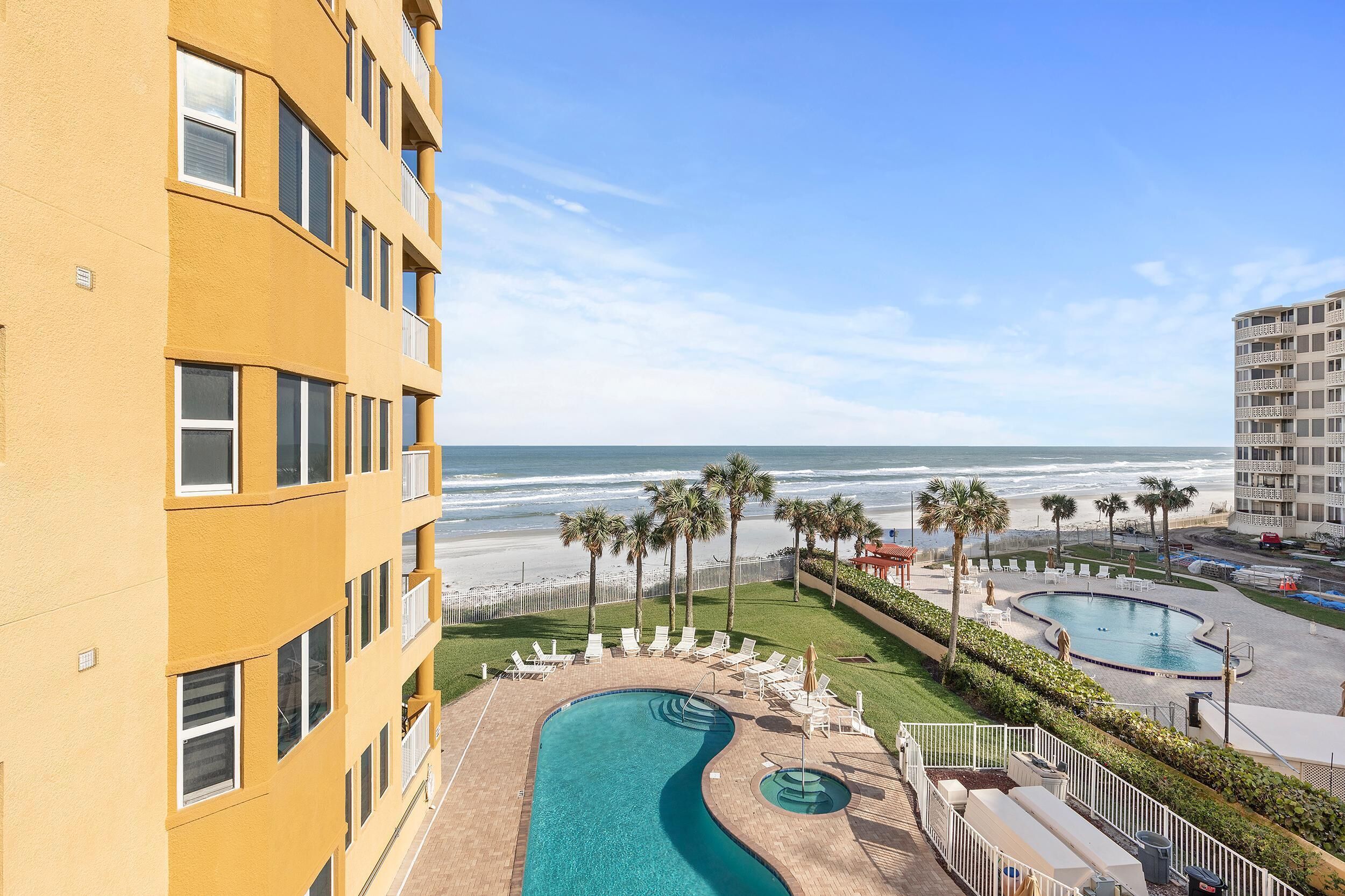 Een hotel met een zwembad, uitzicht op het strand en palmbomen.