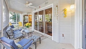 A covered patio with outdoor furniture, a ceiling fan, and a large sliding glass door with a seahorse decoration. - Sea Woods 123 (New Smyrna Beach)
