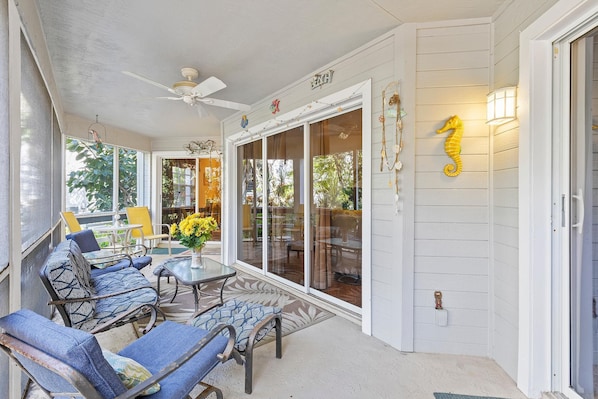 Relax in this serene outdoor seating area, complete with a ceiling fan, glass door, and comfortable seating.