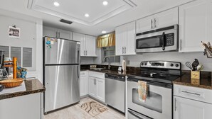 A modern kitchen with stainless steel appliances, white cabinetry, and a granite countertop. - Sea Woods 123 (New Smyrna Beach)