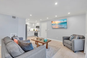 A modern living room with grey sofas, a wooden coffee table, and a kitchen in the background. - Sea Club #25 - Dolphin's Watch (Indian Shores)