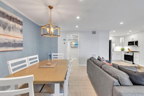 A modern kitchen with white cabinets, a black microwave, and a wooden dining table with white chairs. - Sea Club #25 - Dolphin's Watch (Indian Shores)