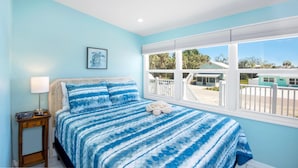 A bedroom with a bed, a nightstand, a lamp, and a window with a view of the outside.