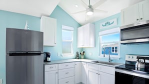 A kitchen with white cabinets, a stainless steel refrigerator, a black stove, and a window with a view of a house.