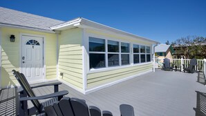 A building with a white door and windows, a covered deck with chairs, and a clear blue sky.