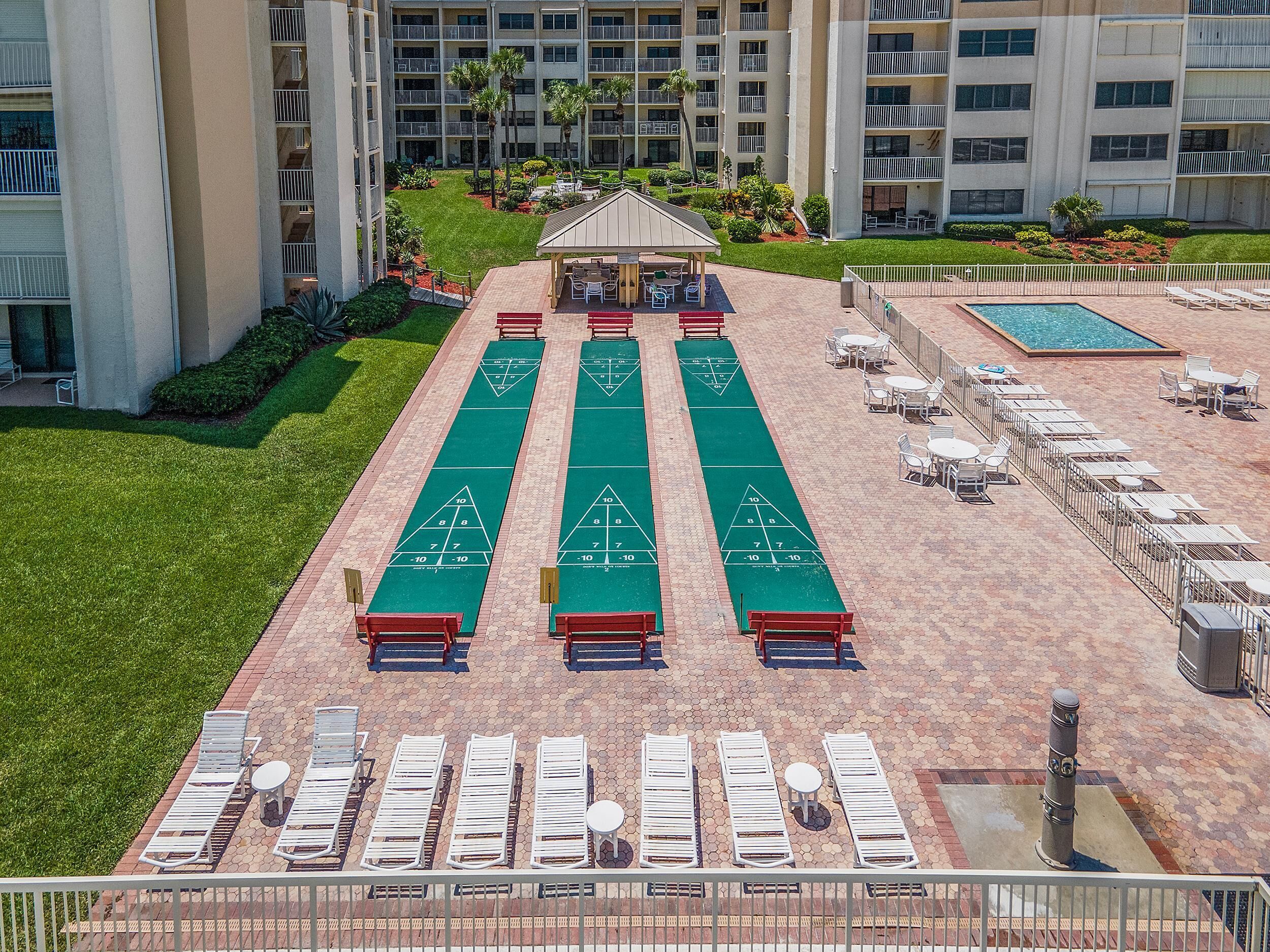 A rooftop pool area with shuffleboard tables, lounge chairs, and a covered seating area.