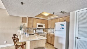 Una cocina con gabinetes de madera, microondas, estufa, refrigerador y un bote de basura.