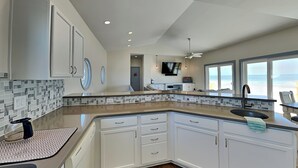 A modern kitchen with white cabinets, a wooden floor, and a large window offering a view.
