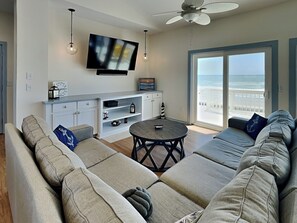 Relax in this spacious living room with a comfortable sofa, flat-screen TV, and sliding glass door leading to a balcony with ocean views.
