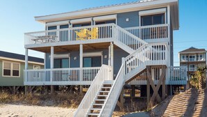 Una casa frente al mar de varios pisos con una terraza de madera y escaleras que dan a los balcones.