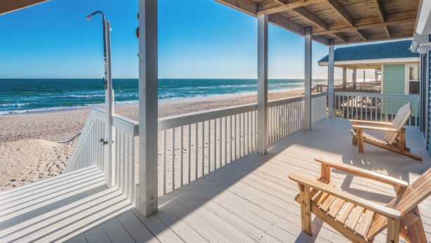Una terraza de madera con vista a la playa y al océano.