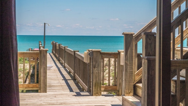 Un paseo marítimo de madera que conduce a una playa con aguas azules y cristalinas.