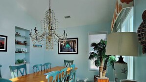 A dining area with a wooden table and teal chairs, a chandelier, and a potted plant. - Clamalot by Topsail Realty (Holly Ridge)