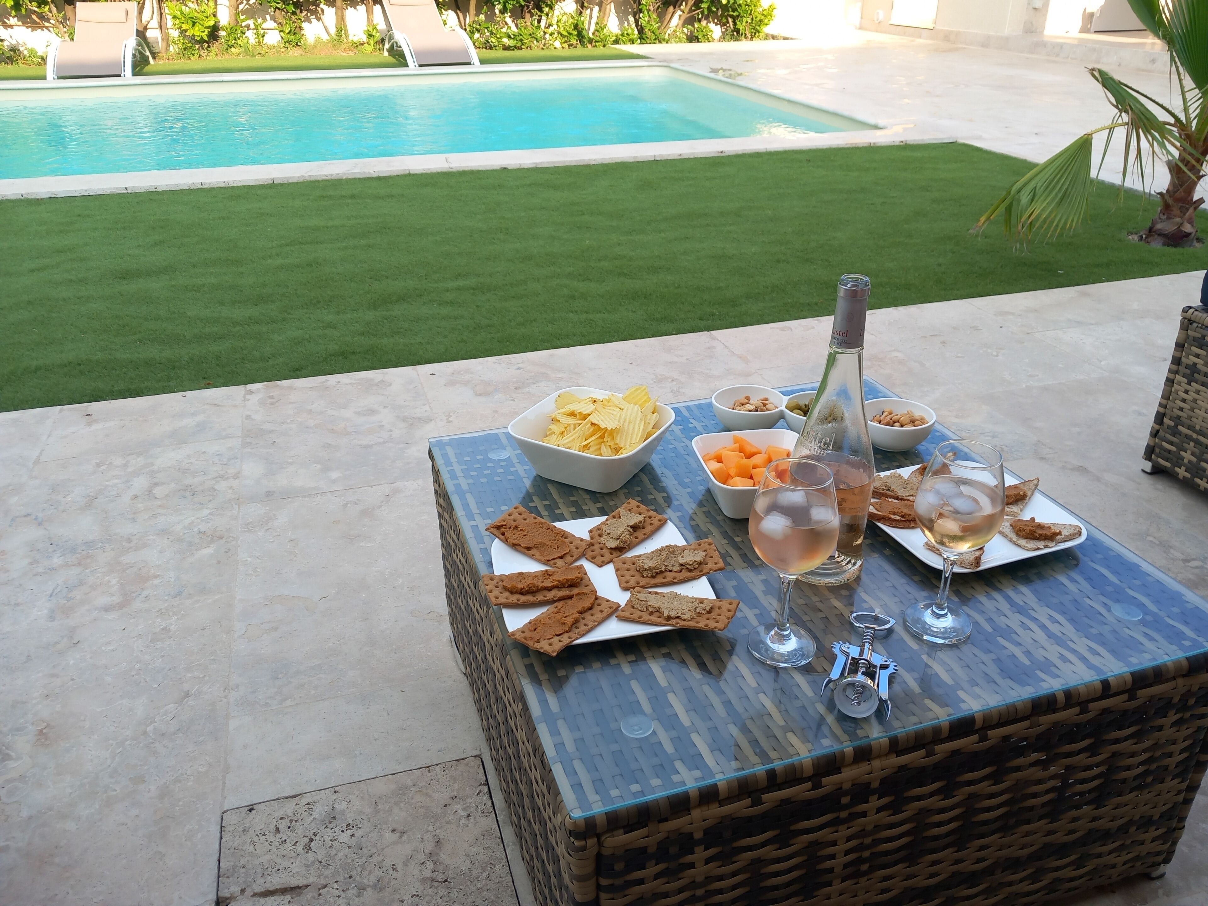 A poolside table with snacks, drinks, and a bottle.