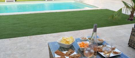A poolside table with snacks, drinks, and a bottle.
