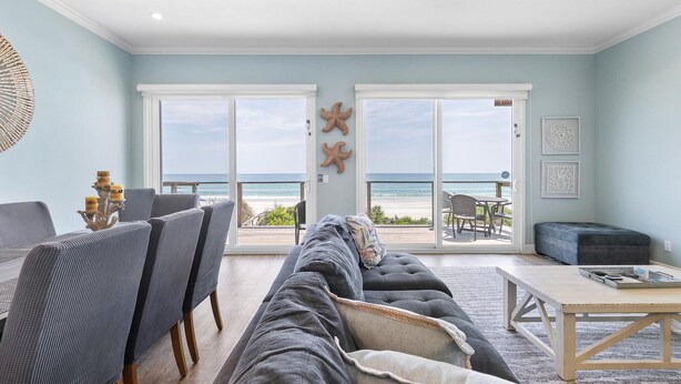 A spacious living room with a large sofa, dining area, and a view of the ocean through sliding glass doors. - Ocean Dream (New Smyrna Beach)