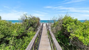 A wooden boardwalk leading to a beach, surrounded by dense green foliage. - Ocean Dream (New Smyrna Beach)