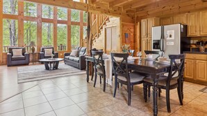 A spacious living area with a large wooden dining table, dark wooden chairs, and a sofa set. A kitchen with wooden cabinets and a refrigerator is visible in the background. - Amazing Views Hot Tub Game Room Pool (Gatlinburg)