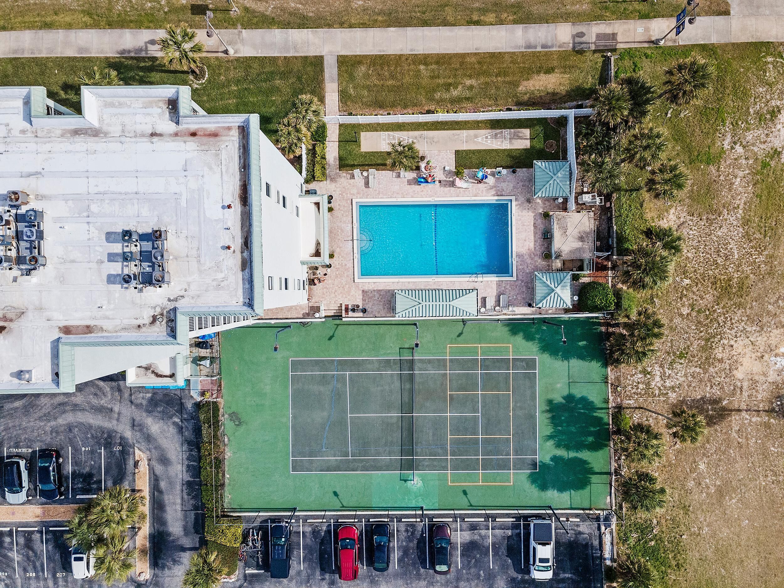Vista aérea de una propiedad con piscina, cancha de tenis y zona de estacionamiento.