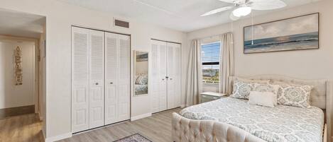 Un dormitorio con una cama grande, un ventilador de techo y vista al océano a través de una ventana.