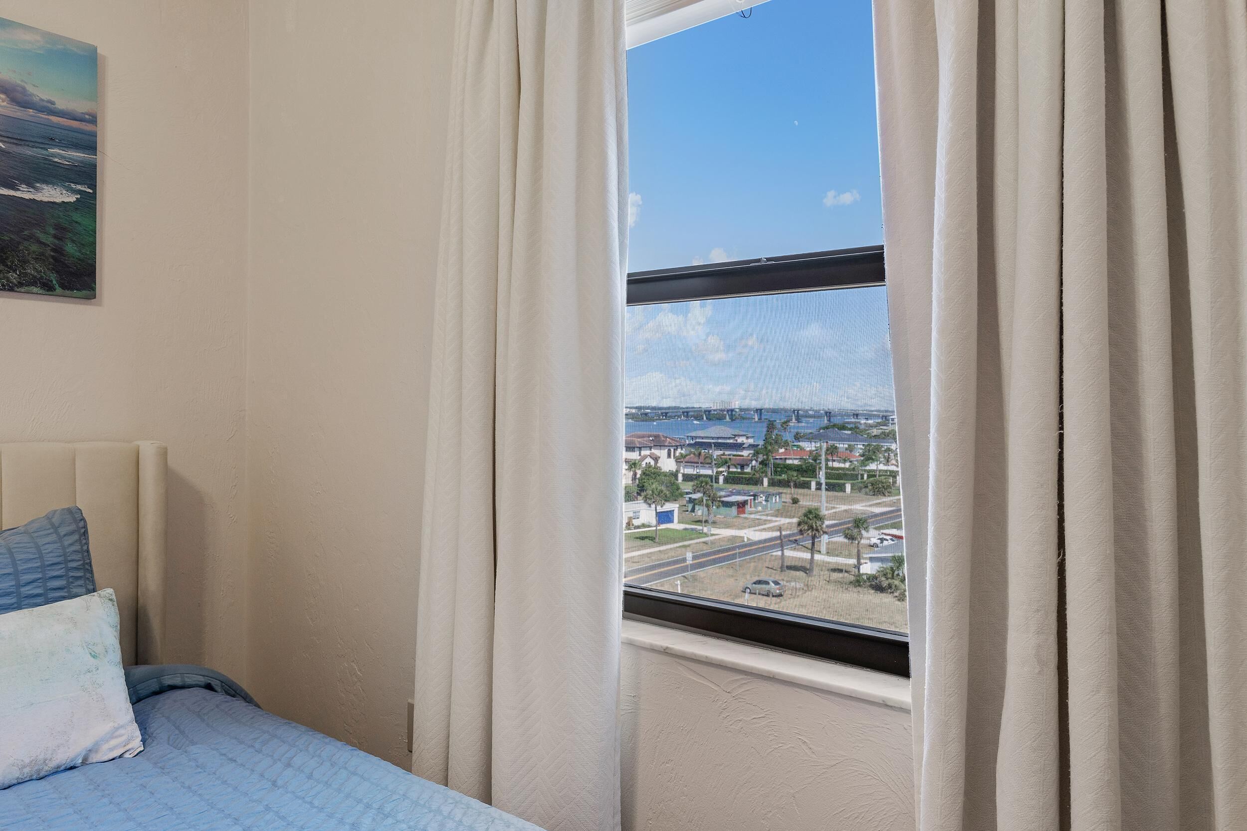 Un dormitorio con cama, ventana con cortinas y un cuadro en la pared.
