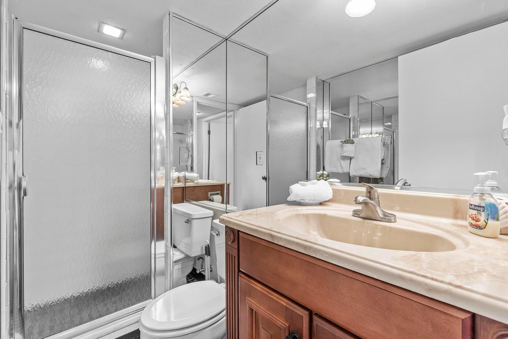 Un baño moderno con cabina de ducha de vidrio, un lavabo con encimera color beige y un espejo grande.