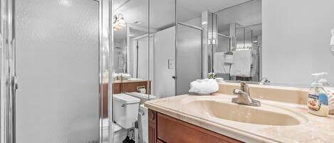 Un baño moderno con cabina de ducha de vidrio, un lavabo con encimera color beige y un espejo grande.