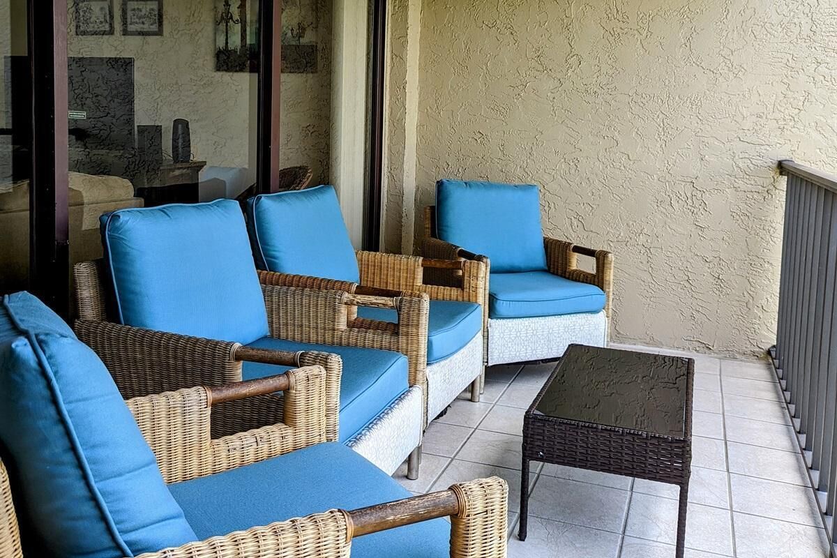 A patio with wicker furniture and blue cushions, a small table, and a view of the interior through a glass door.