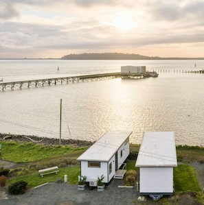 A waterfront property with a dock extending into the water, a small white building, and a larger white structure with a flat roof.