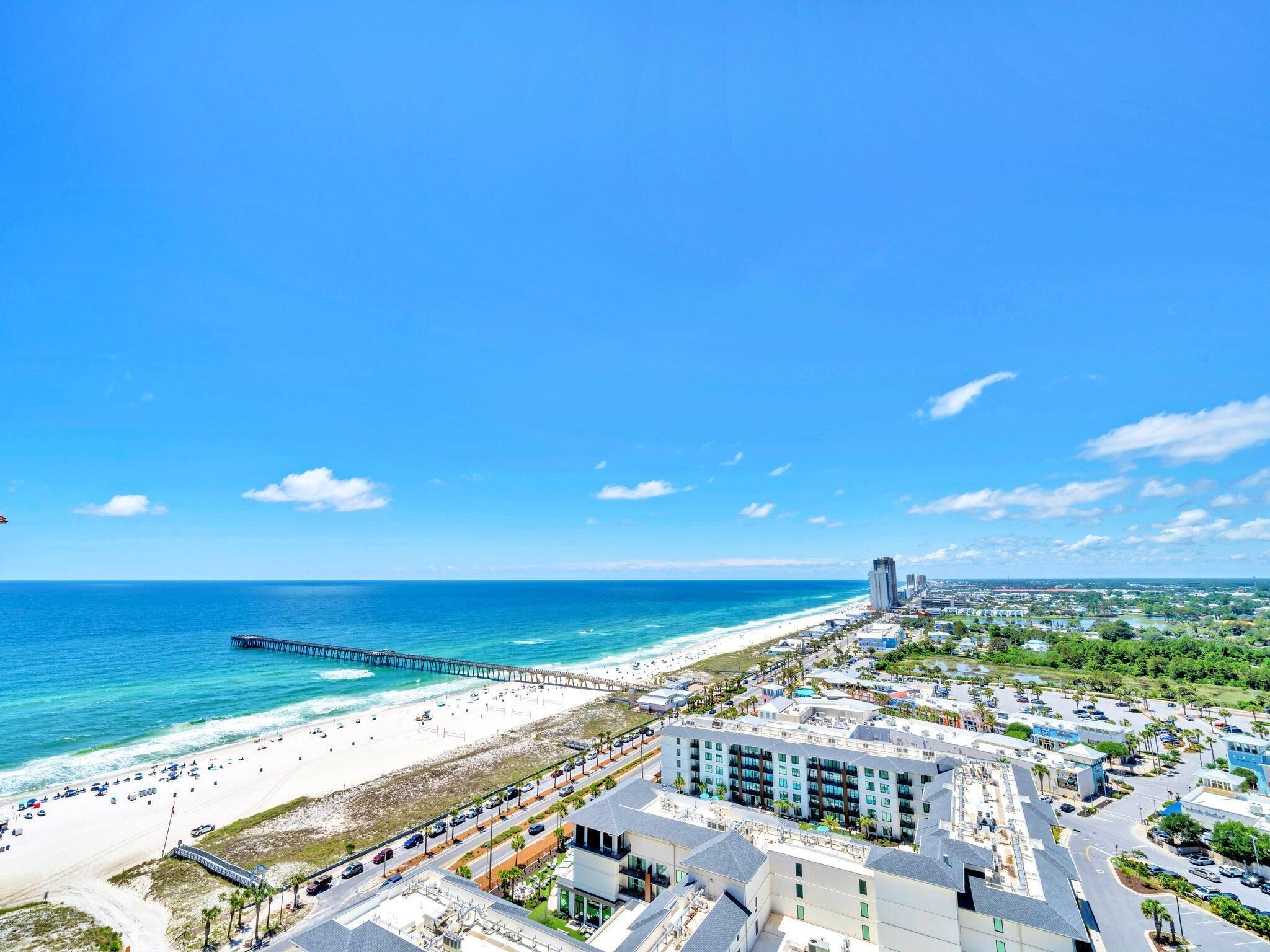 A coastal cityscape with a beach, a pier, and a hotel with multiple floors and balconies.