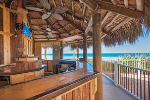 Zona de bar de fusta amb teulada de palla, amb vista a una platja.