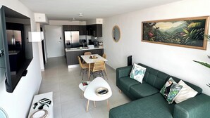 Een moderne woonkamer met een groene bank, een eethoek met een witte tafel en een keuken met donkere kasten.