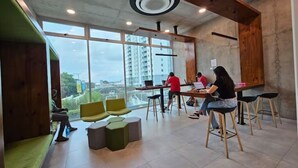 Een modern interieur met een hoge plafond, grote ramen en een zithoek met krukken en een bank.