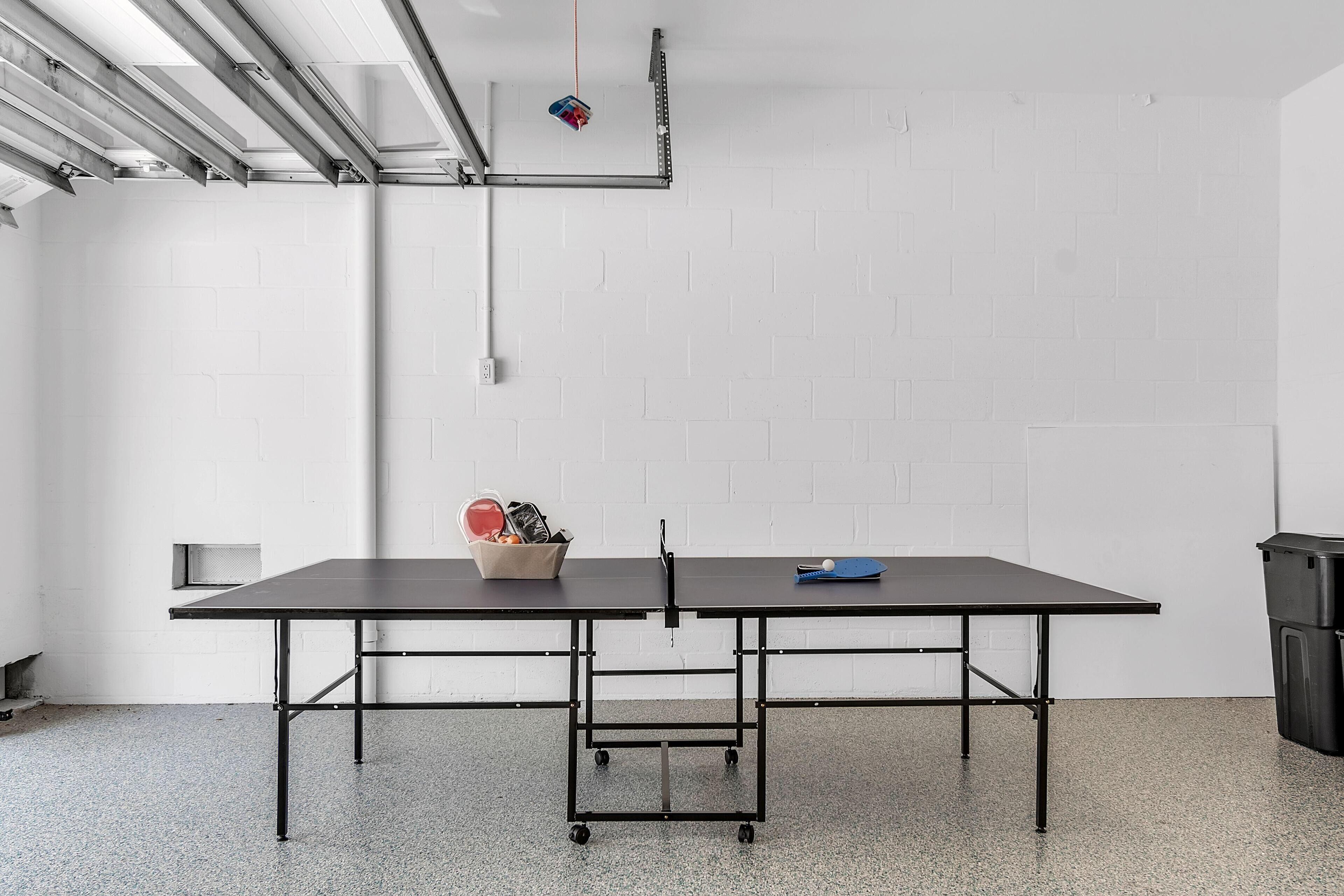 Une pièce avec une table noire, des murs en briques blanches et un plafond avec des poutres apparentes et un objet suspendu.