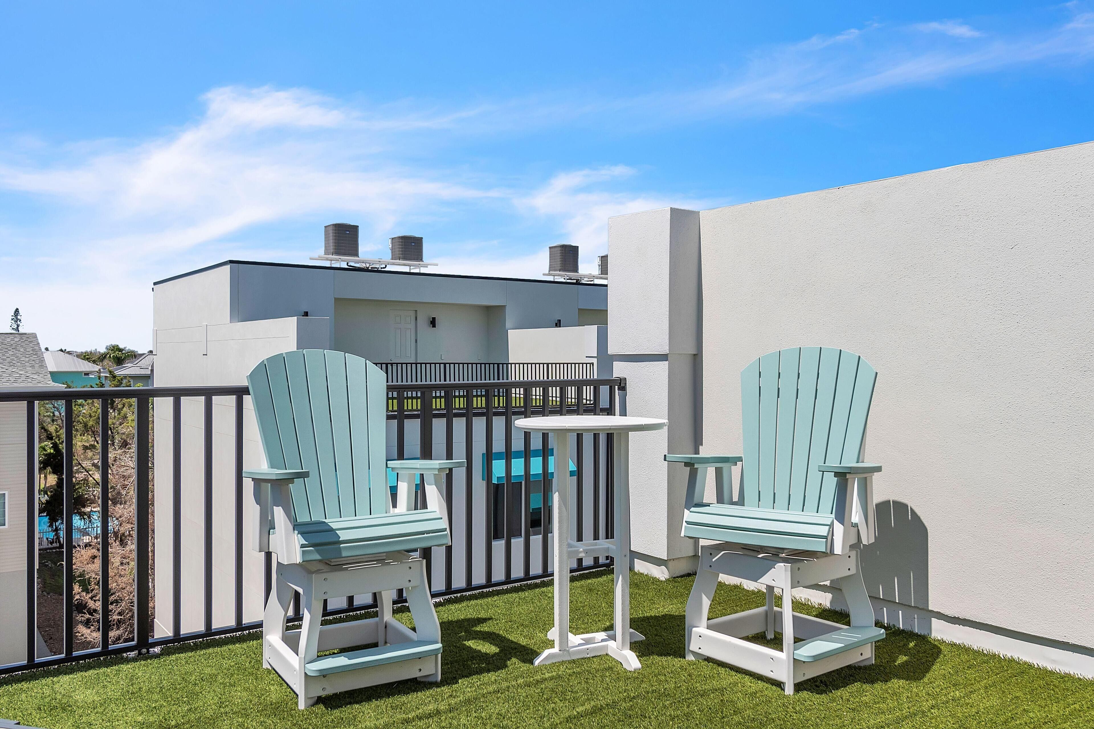 A patio with two Adirondack chairs and a small table, surrounded by a white wall and a black fence.