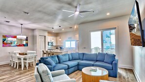 Un salon moderne avec un canapé d’angle, une table basse et un coin repas comprenant une table et des chaises blanches.