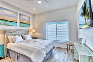 Un dormitorio con cama, mesitas de noche, escritorio, ventilador de techo y obras de arte en las paredes.