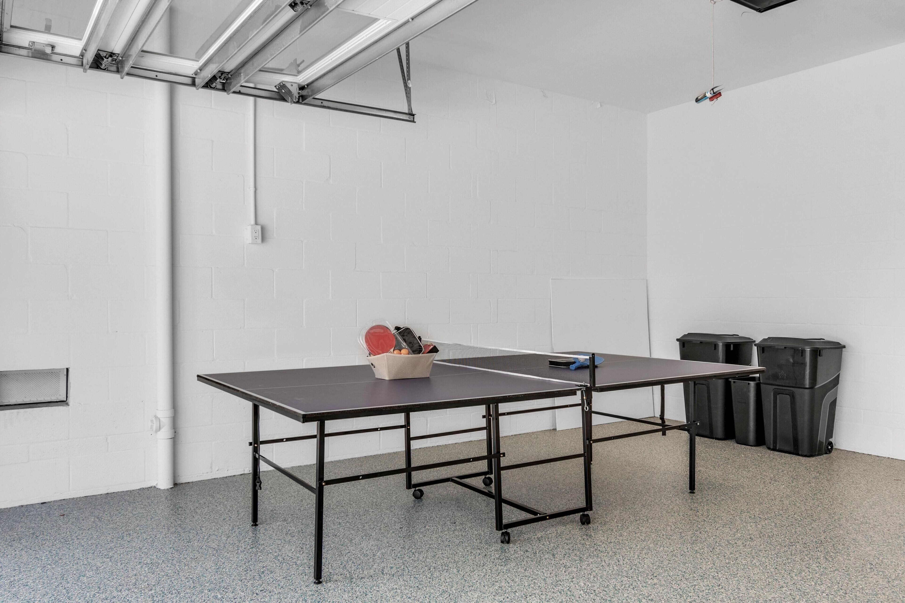 A ping pong table in a room with white brick walls, a white ceiling, and a grey floor. There are two trash bins against the wall.