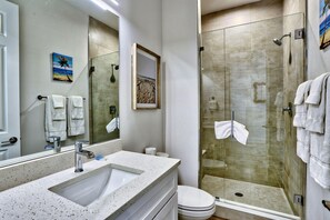 Un baño con lavamanos, espejo y ducha con mampara de vidrio.