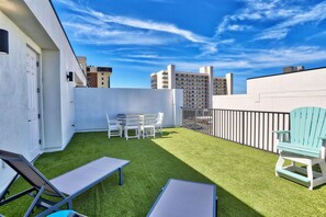 Una terraza en la azotea con césped artificial, una mesa con sillas y un sillón Adirondack azul.