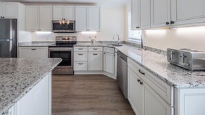 A modern kitchen with white cabinets, a stainless steel refrigerator, a built-in oven, a microwave, a sink, and a toaster. - Bear's Den by Topsail Realty (Holly Ridge)